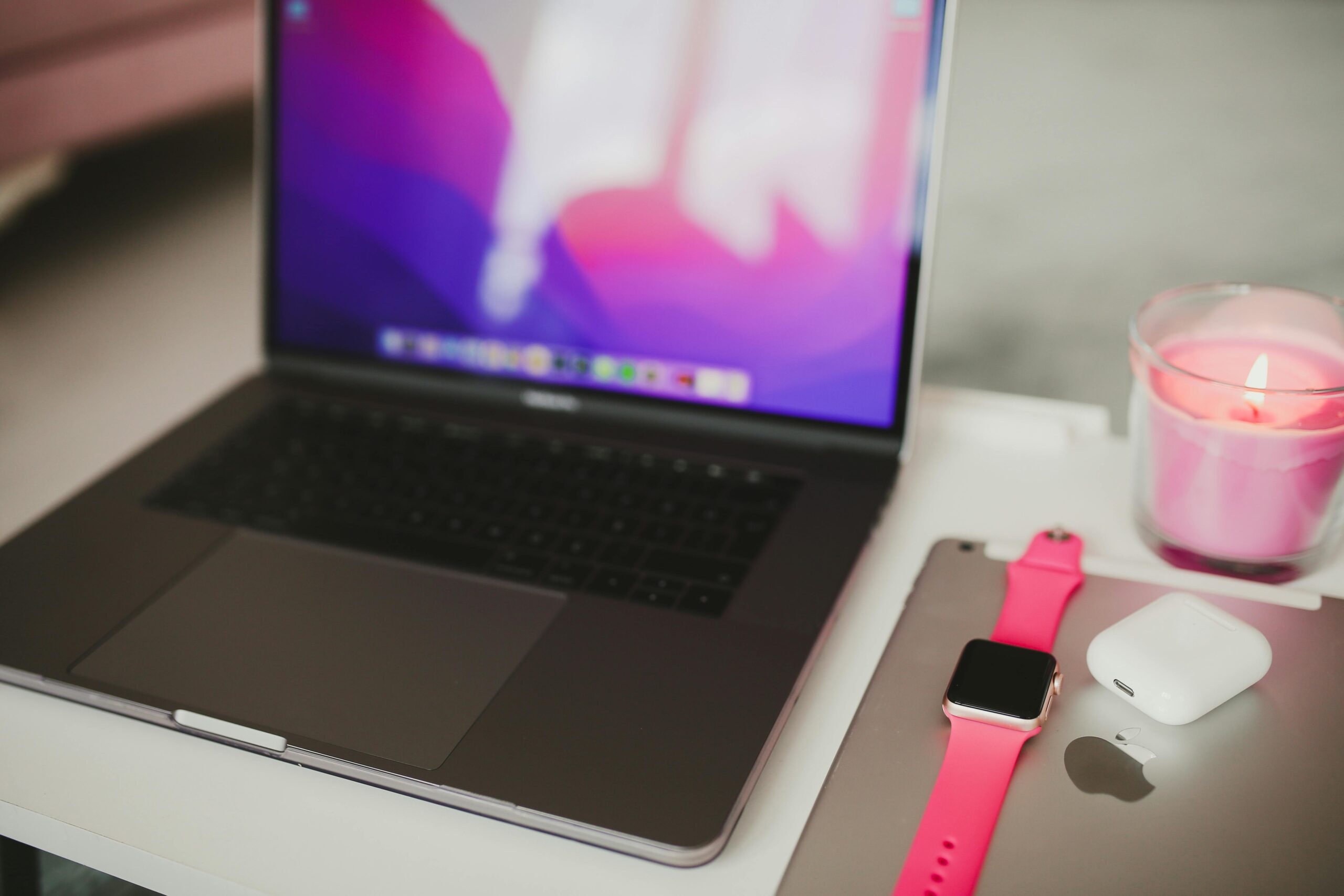 Cozy workspace setup featuring a laptop, smartwatch, and a lit candle offering a warm ambiance.